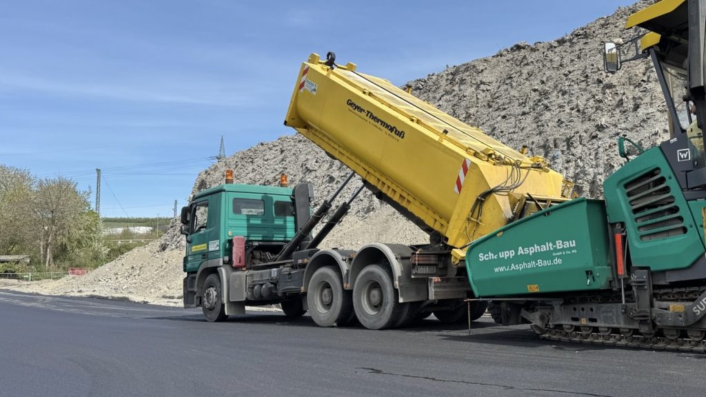Grüner LKW von Schaupp Asphalt-Bau mit gelbem Thermocontainer beim Asphaltantransport auf einer Baustelle in Hammelburg